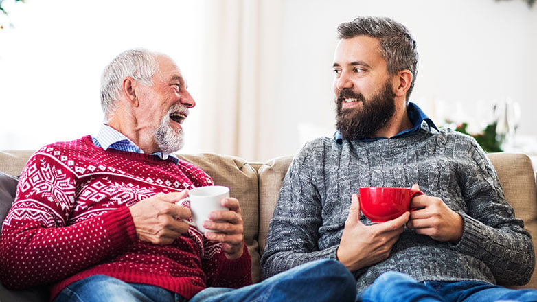 Father and son on the couch having coffee and catching up with each other.