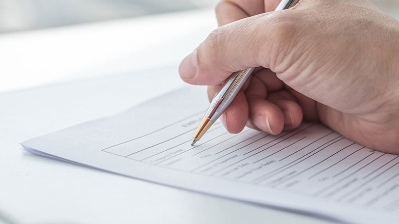 A hand with a pen filling out an application