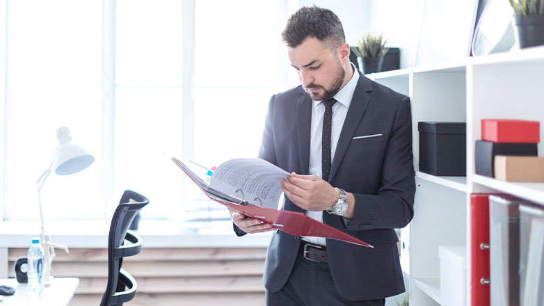 man standing by desk paging through binder