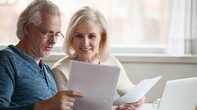 older couple finalizing paperwork at desk with computer