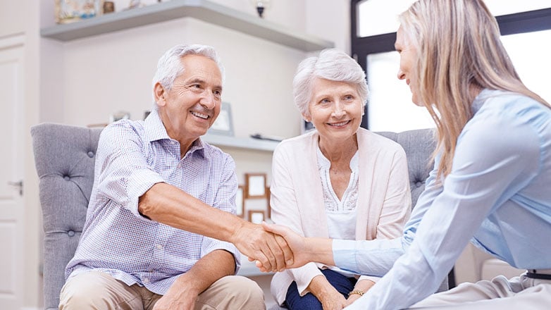 older man and woman shaking hands with woman across table