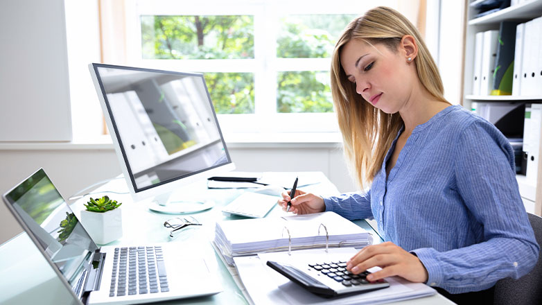 woman comparing numbers on calculator and two computers