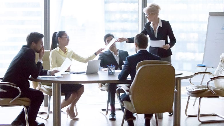 woman handing out papers to employees around table