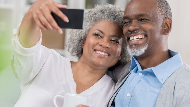 Older couple smiling together taking a selfie with their phone.