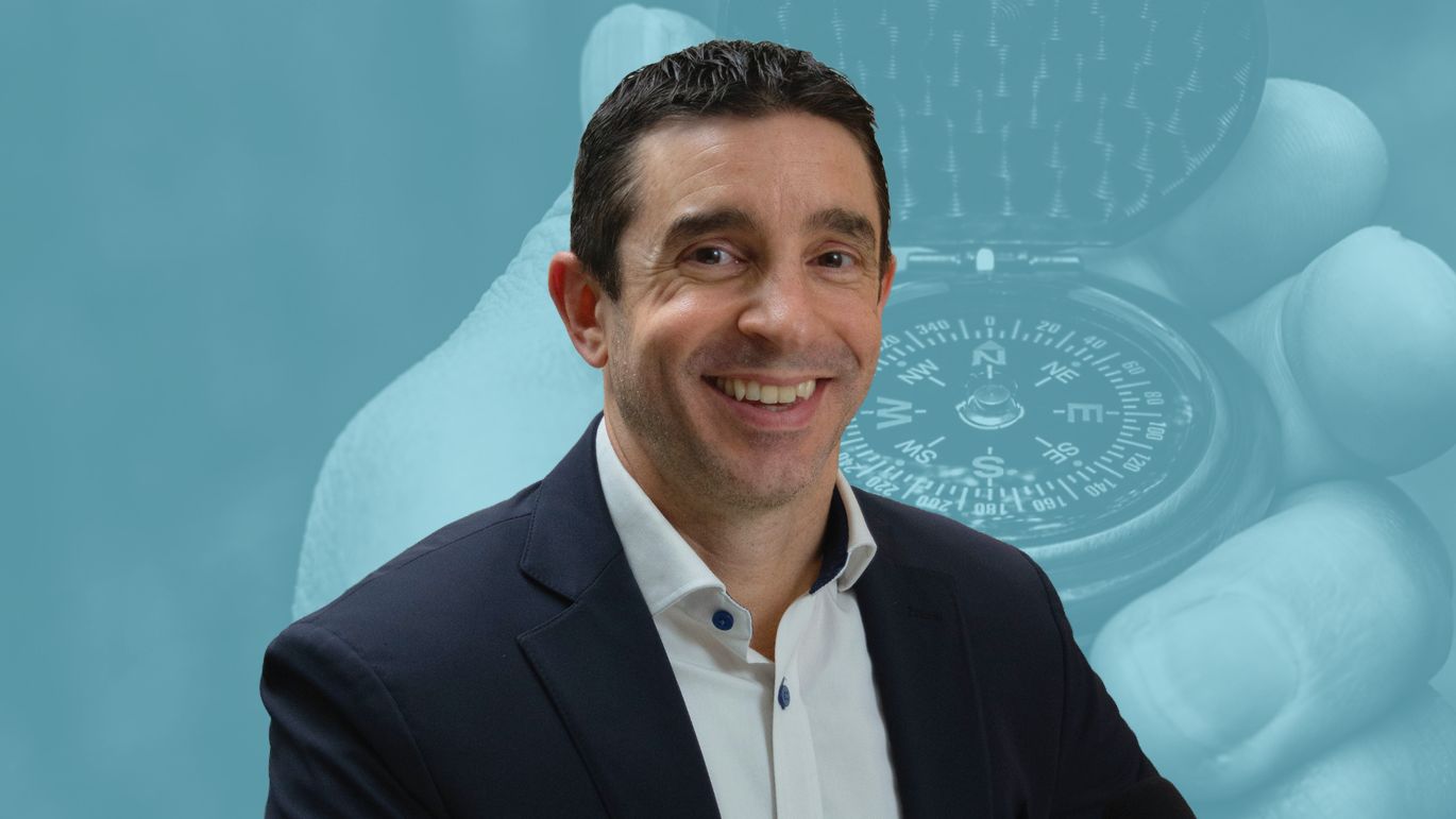 Person in business attire seated in front of a blue-toned background featuring a compass.