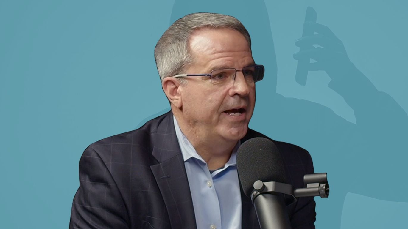 Person speaking into a microphone against a blue-toned background featuring a smartphone silhouette.