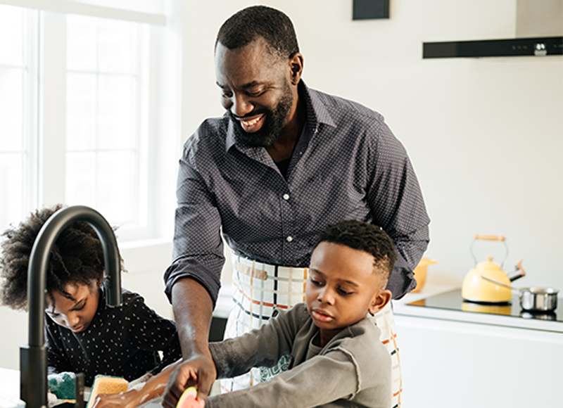 african american dad washing dishes with kids after a meal.