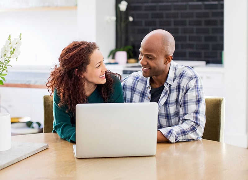 Husband and wife view a document on a laptop together in their home.