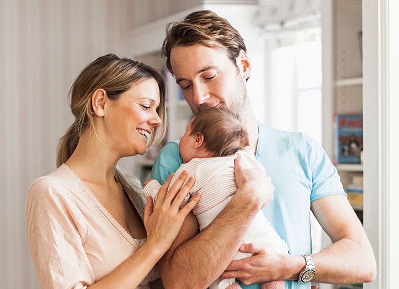 Young couple hold their newborn baby together in their home.