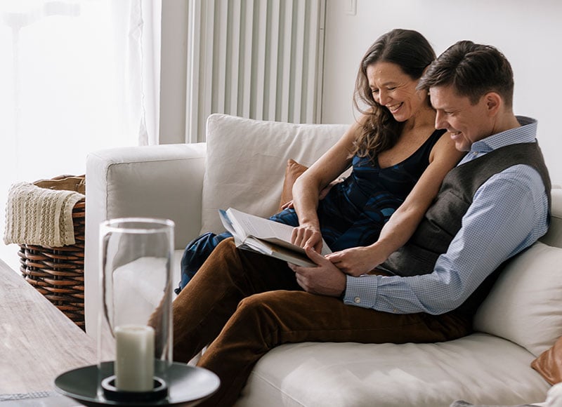 Young couple is sitting on a couch in their living room and looking at a book together.