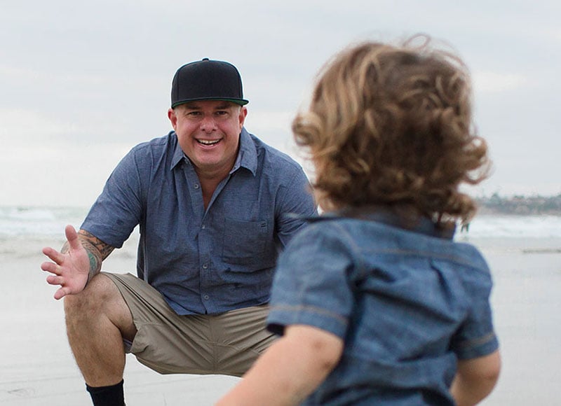 Dad waiting for toddler son to run to him on a beach.