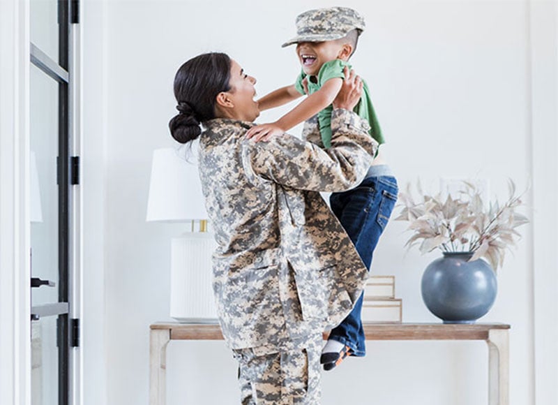 Military mom holding son in the air.