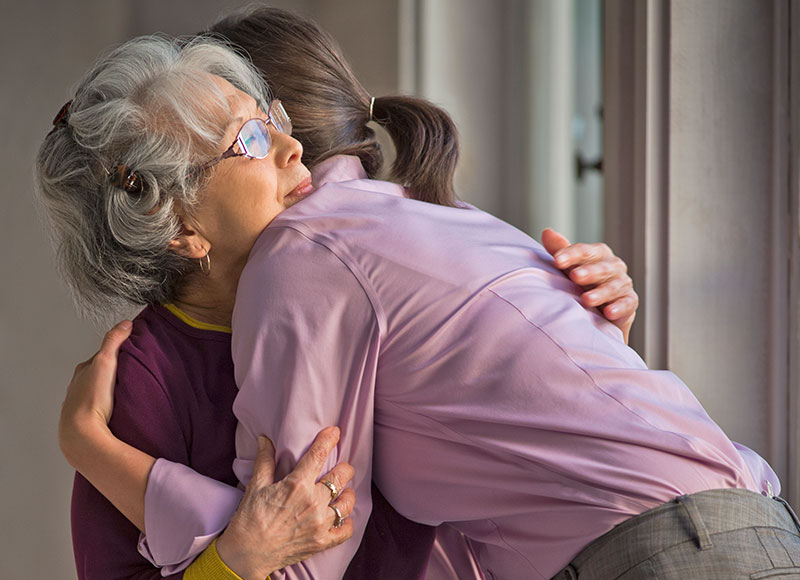 Daughter consoles her elderly mom with a hug after her husband passes away.