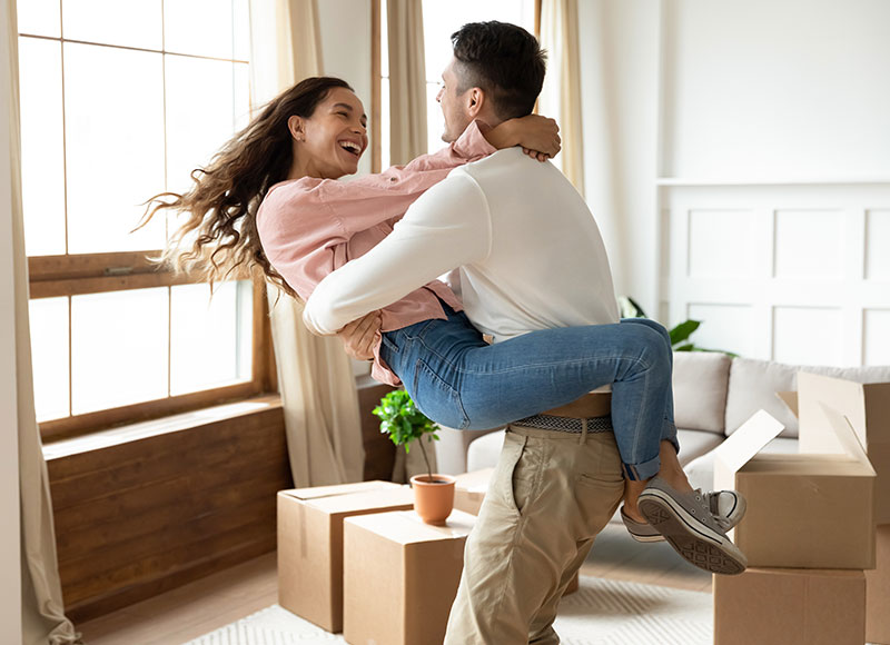 Husband happily twirls his wife around in the living room of their new home.