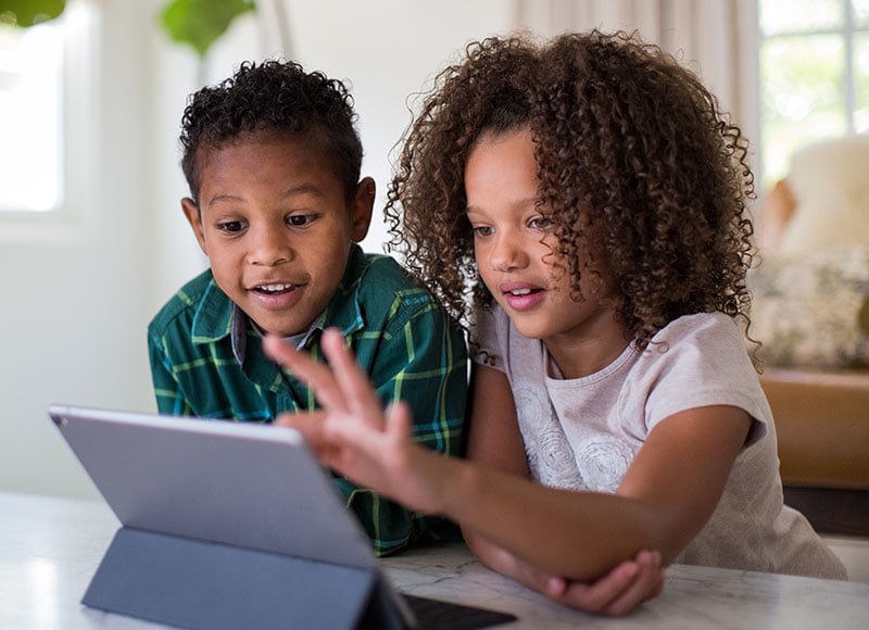 A young brother and sister look at a tablet together.