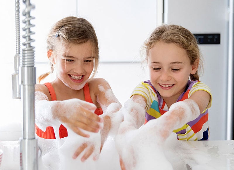 Two young girls have fun washing dishes with soapy water.
