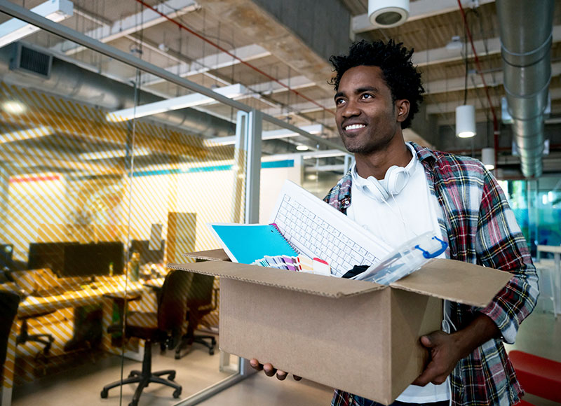 Young man carries his box of office supplies into his new workplace.