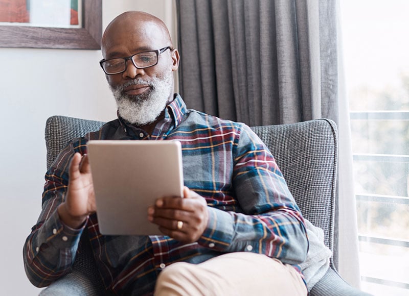 Older man sitting in armchair looking at his tablet.