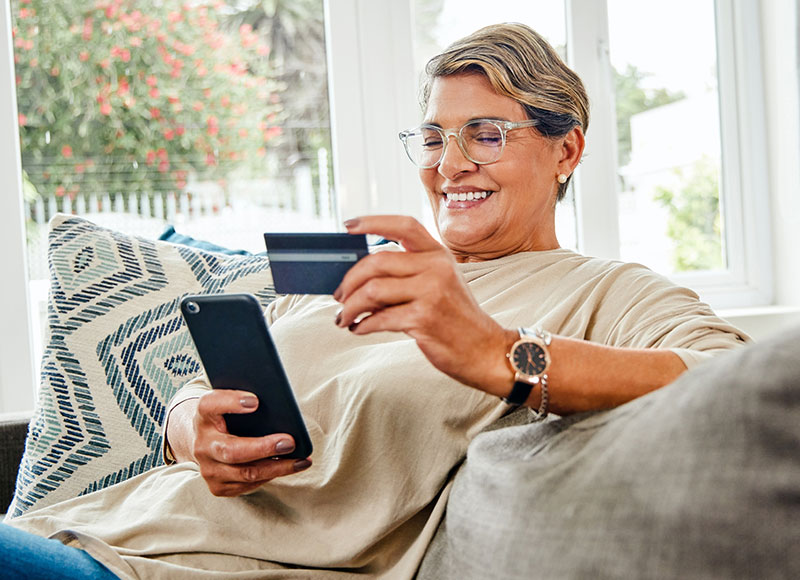 Mature woman making a purchase on her phone with her debit card.