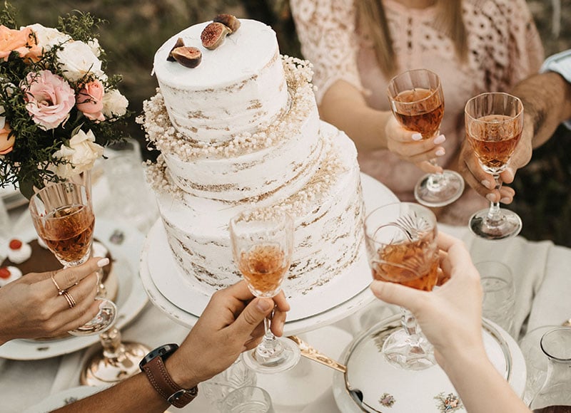 Wedding guests gather around a wedding cake and hold glasses of champagne.