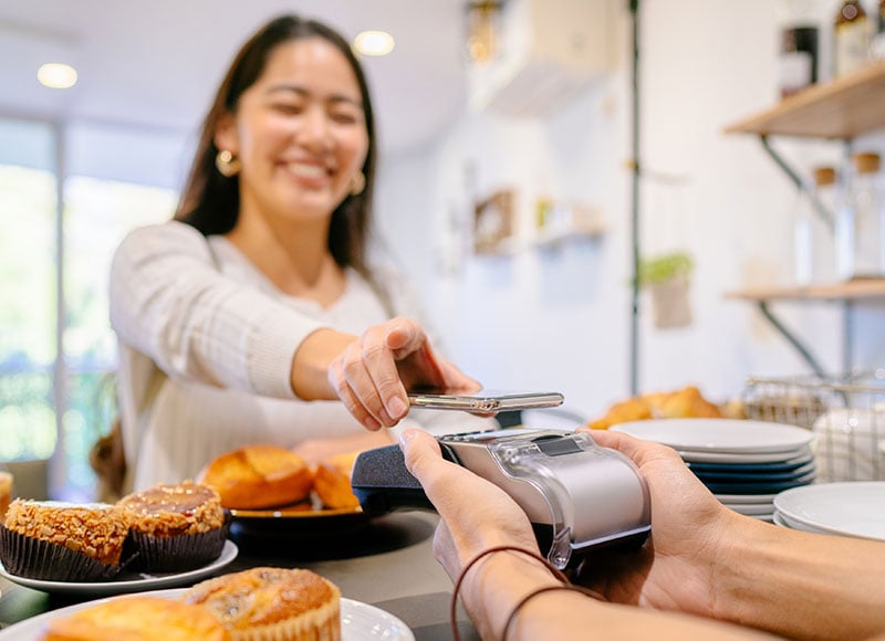 Woman uses smartphone to pay for her goods from a bakery.