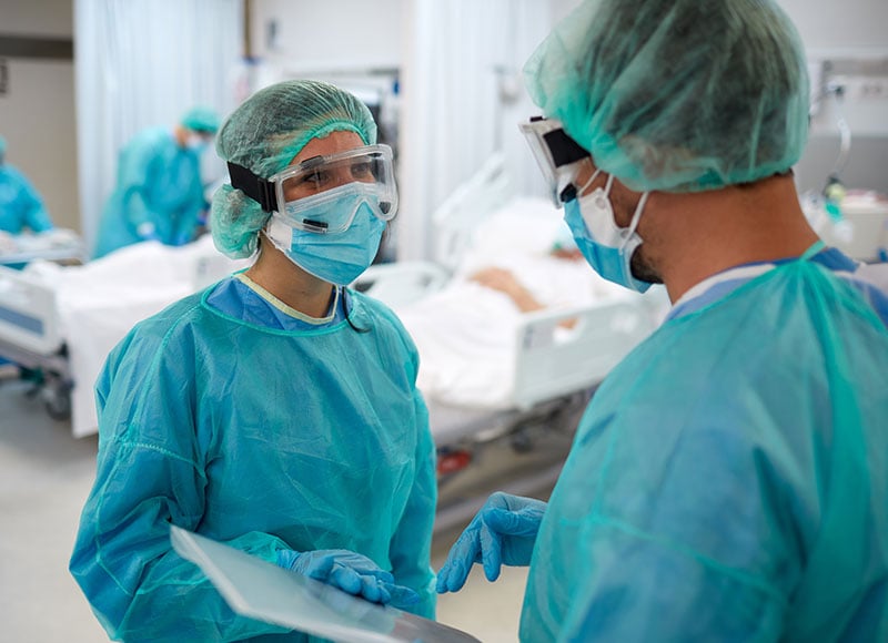 Two surgeons in the operating room discuss a patient's charts.