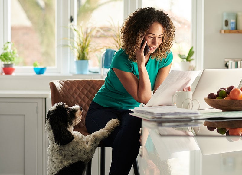 Woman talks on the phone while checking her computer in her kitchen.