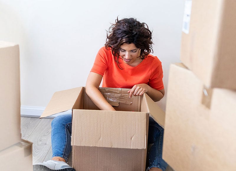 Woman sitting on floor of her new home and unpacking boxes.