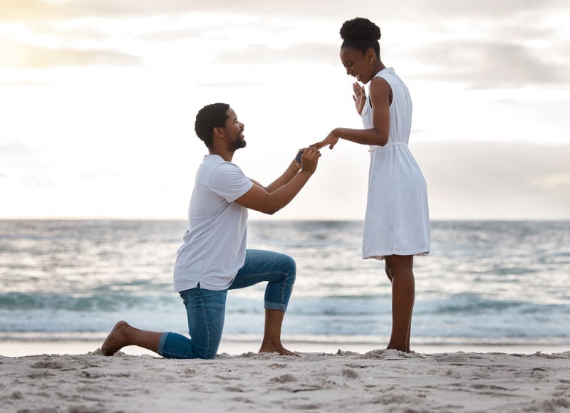 Young man proposes to his girlfriend on the sandy beach at sunset.