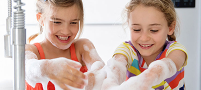Two young girls have fun washing dishes with soapy water.