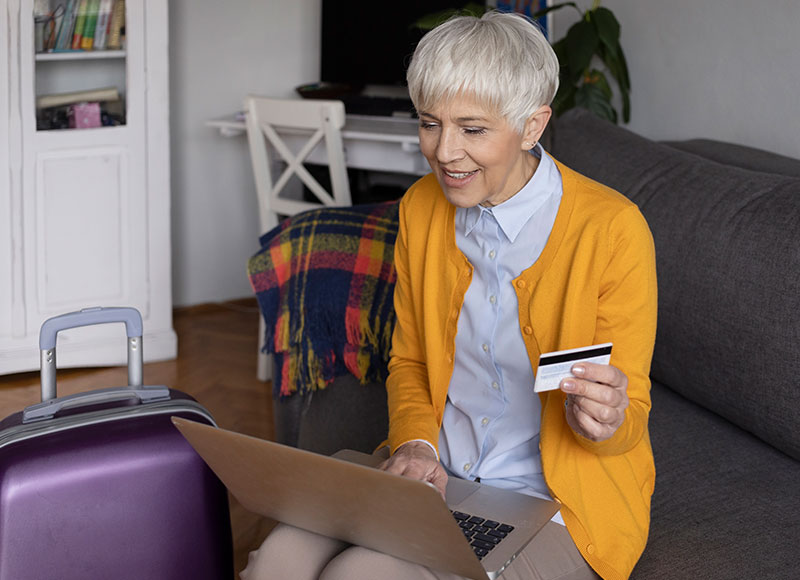 Elderly woman books a flight online using her credit card.