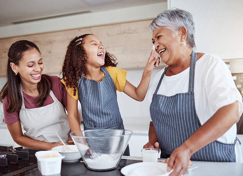 Grandma, mom, and granddaughter happily bake cookies together.
