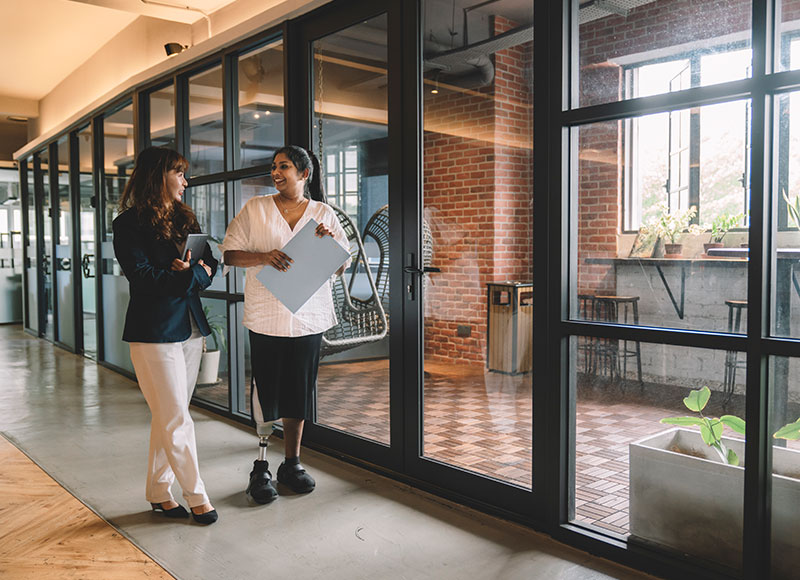 Work colleagues walk down the hallway of their workpace together.