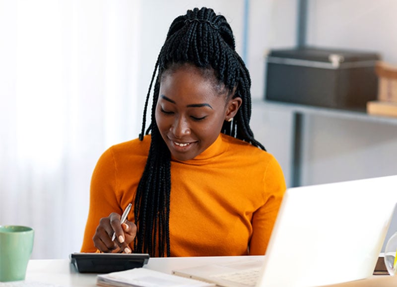 Woman uses a calculator while doing accounting work on her work laptop.