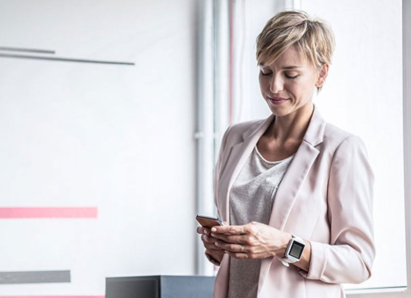 Female professional standing in her office looking at her phone.