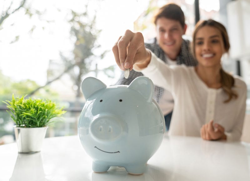 Young couple putting coins into a piggy bank.