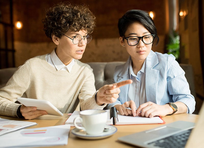 Female business colleagues work together on a project in a coffee shop.