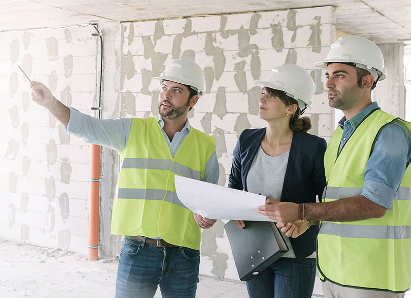 Business owner and architects wear hard hats and meet at a construction site.