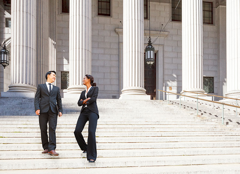 Two lawyers walk down the steps of a courthouse.