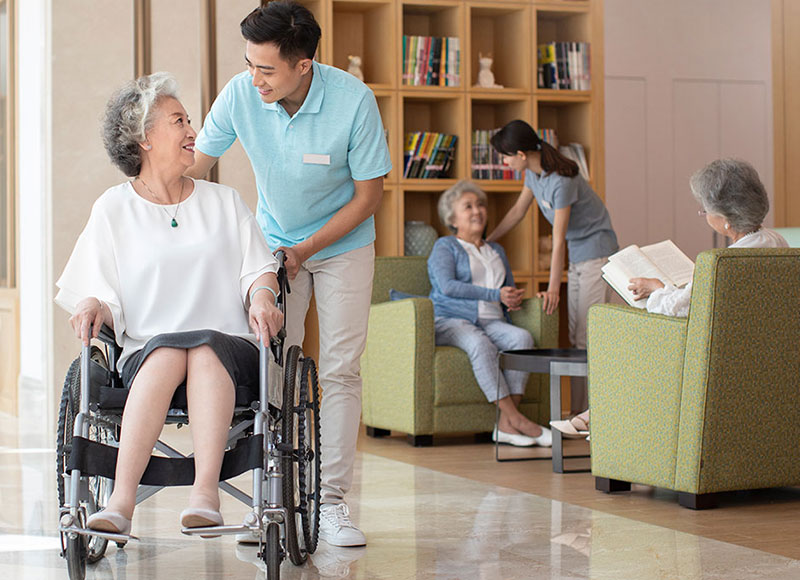 Attendant pushes elderly woman in a wheelchair in a nursing home.